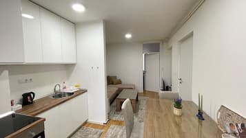 Une cuisine de taille réduite avec des meubles blancs, un évier et une cuisinière. On y trouve également un coin repas avec une table et des chaises en bois.