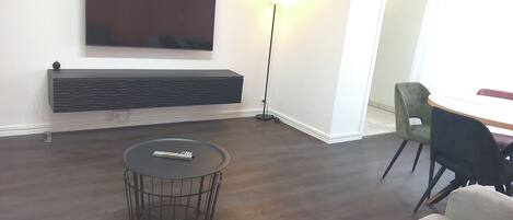 A modern living room with a flat-screen TV mounted on the wall, a standing floor lamp, a round coffee table, and a sofa.