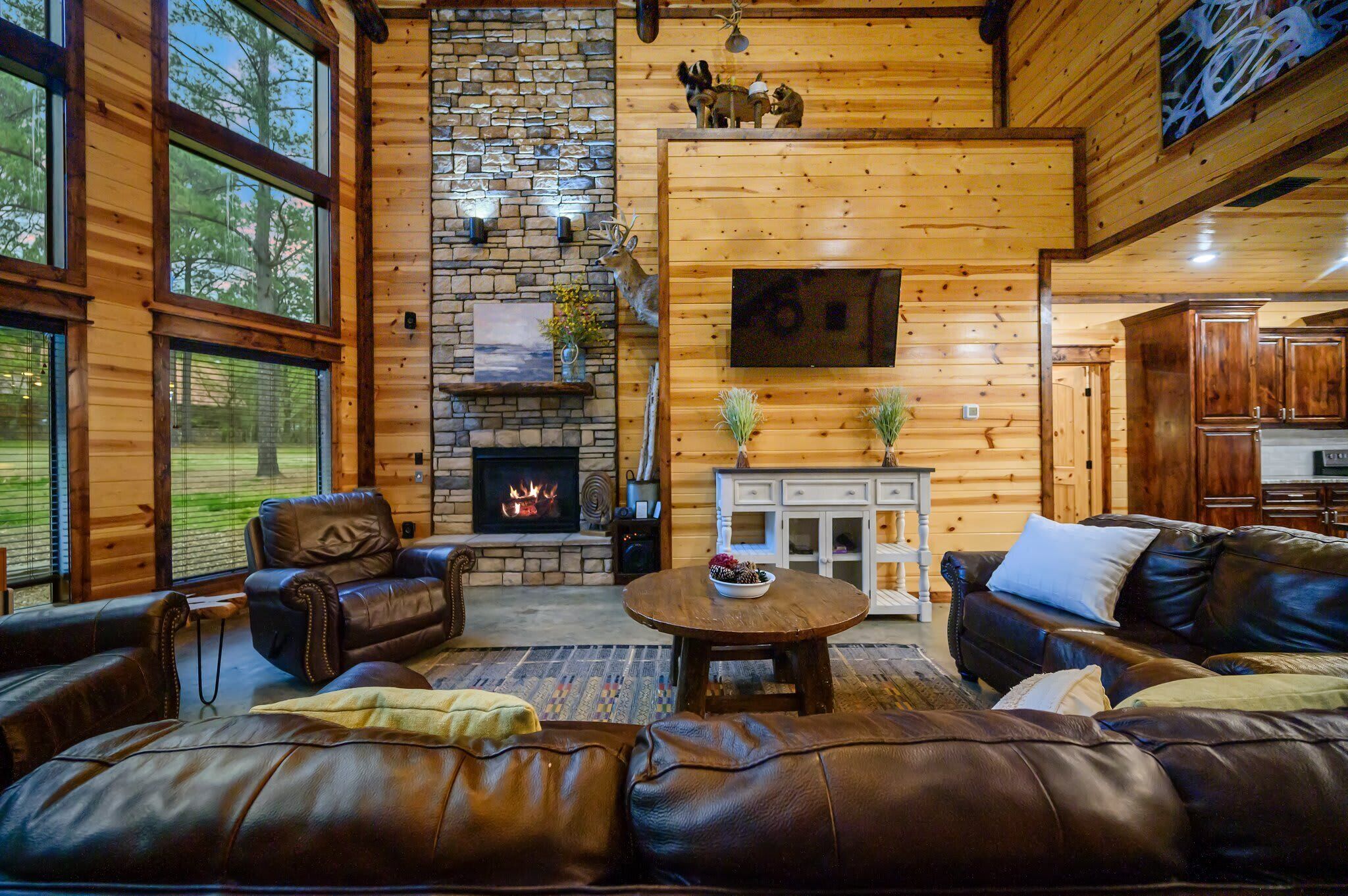 A cozy log cabin interior with leather sofas, a fireplace, and a stone wall.