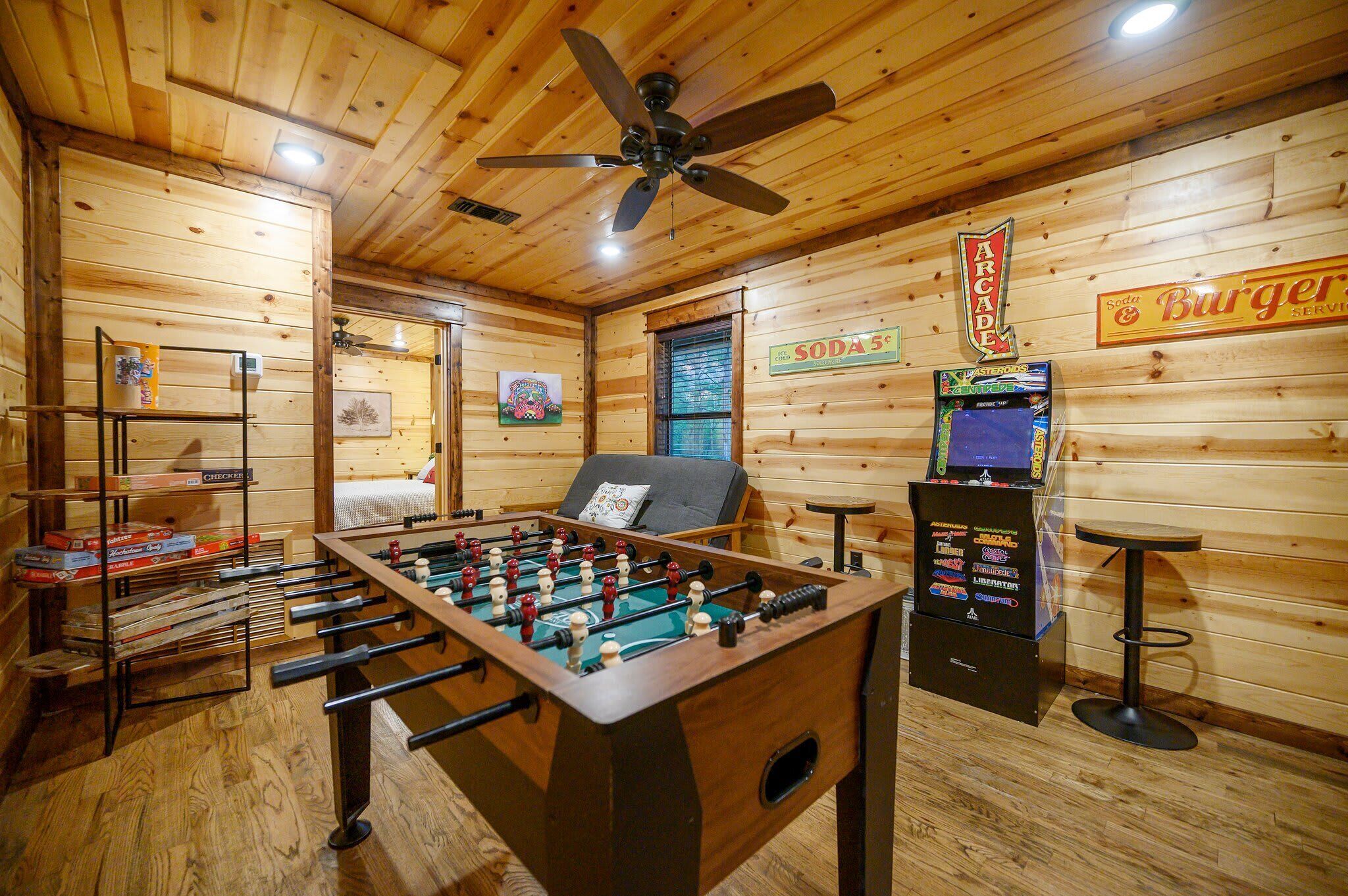 Una habitación con mesa de futbolín, ventilador de techo y máquina expendedora de refrescos.