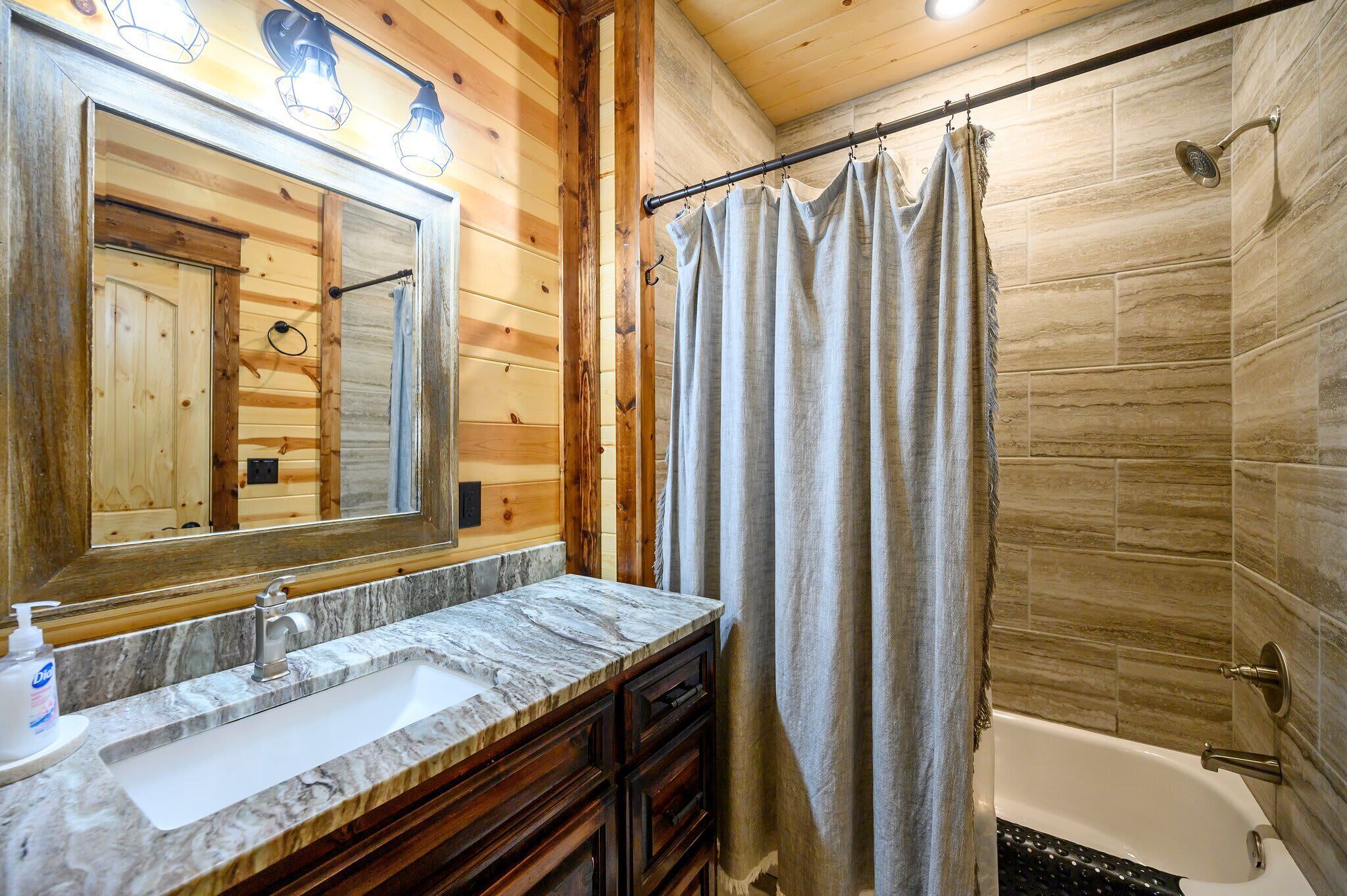 A bathroom with a wooden vanity, a large mirror, a bathtub, and a shower curtain.