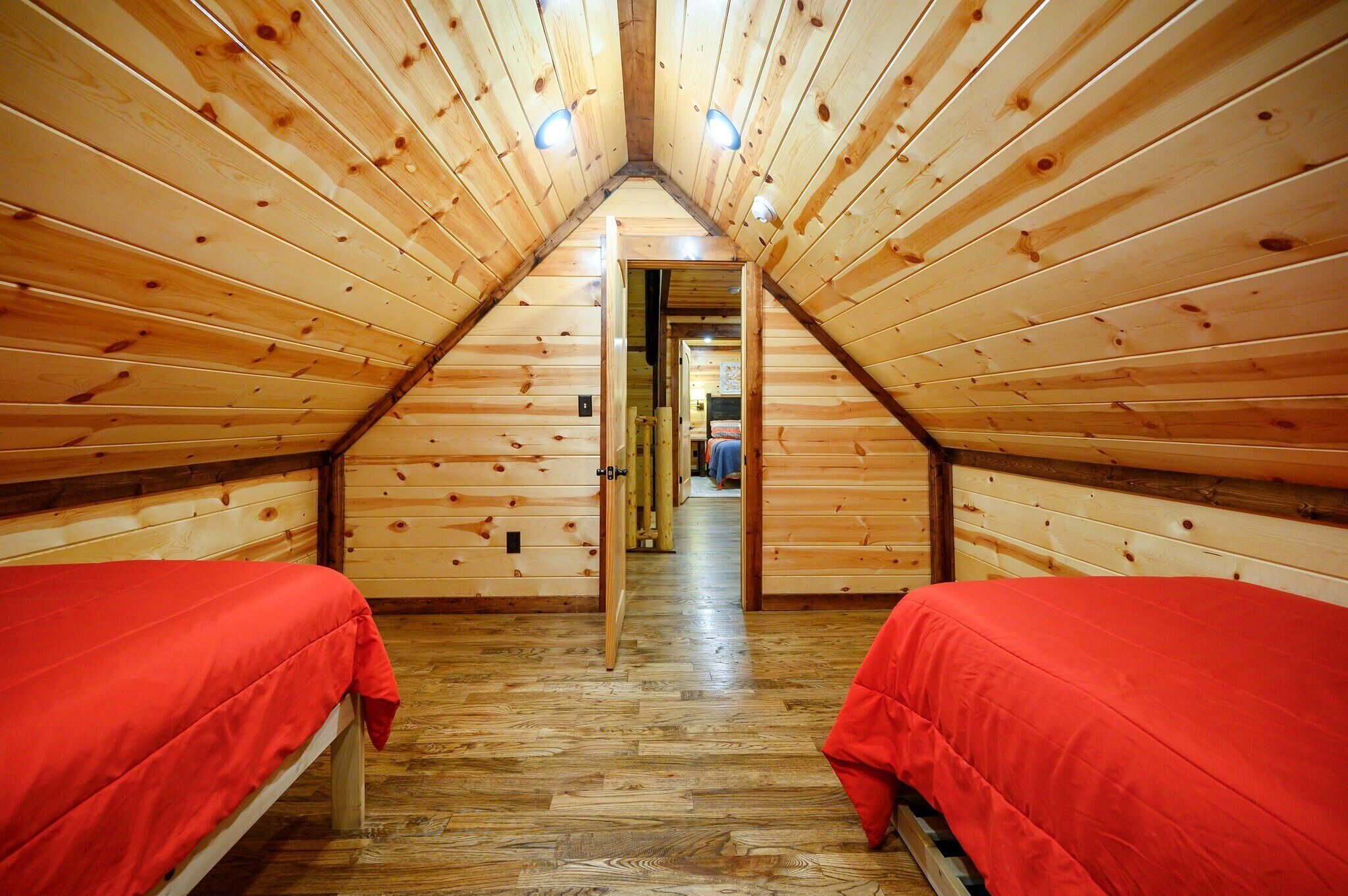 Een houten chalet met twee bedden, een schuine kap en een gang die naar een andere kamer leidt.