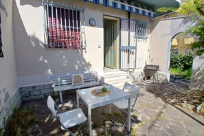 A patio with a table and chairs, a bench with a cushion, and a gate. - CN009 - Cesenatico, new two-room apartment with garden and parking space (Cesenatico)