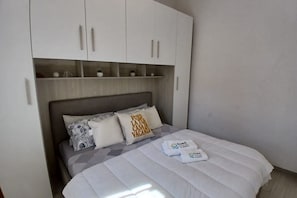 A bedroom with a bed, pillows, a headboard, and a wardrobe with shelves. - CN009 - Cesenatico, new two-room apartment with garden and parking space (Cesenatico)