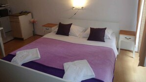 A neatly made bed with a purple bedspread and white linens, two bedside tables with lamps, a small desk with a computer, and a wall-mounted light fixture. - Studio with air conditioning (Rovinj)