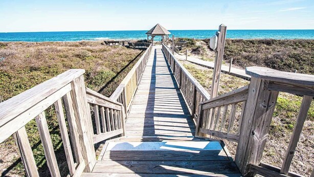 A wooden boardwalk leading to a beach with a gazebo at the end.