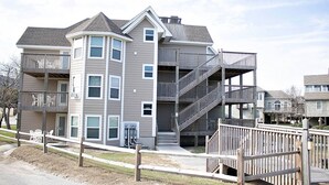 A multi-story residential building with balconies, a covered outdoor area, and a wooden deck. - 1BR Coastal Condo w/ Pool Access (Kitty Hawk)