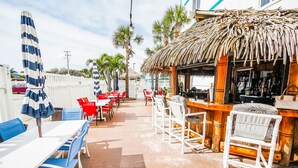 An outdoor seating area with tables and chairs, a bar, and a thatched-roof structure.