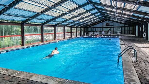 Een binnenzwembad met helderblauw water, een overdekt dak en een betegelde vloer.