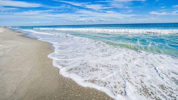 A beach with clear blue water and a sandy shore.