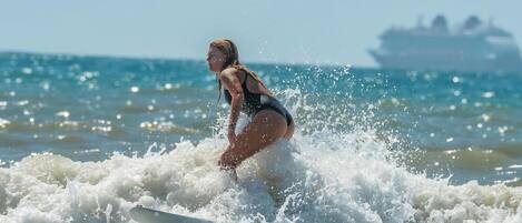 A person surfing on a wave with a ship in the background.