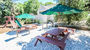 Une cour arrière avec des tables de pique-nique, un toboggan et une maison en arrière-plan.
