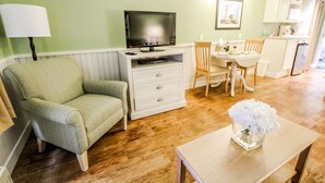 Un salon avec un téléviseur, une table à manger avec des chaises, un petit coin cuisine et un plancher en bois.