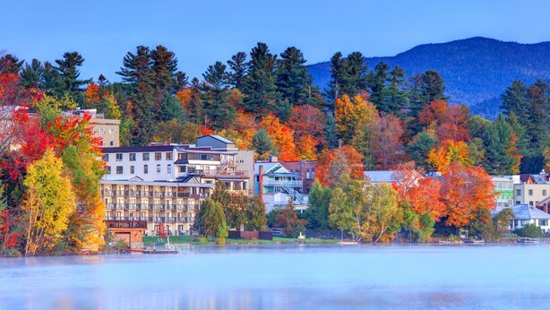 Une ville au bord d’un lac, avec des immeubles à plusieurs étages, un quai et un feuillage automnal.
