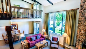 Un salon spacieux avec un haut plafond, une cheminée, un coin repas et une vue sur l’extérieur.