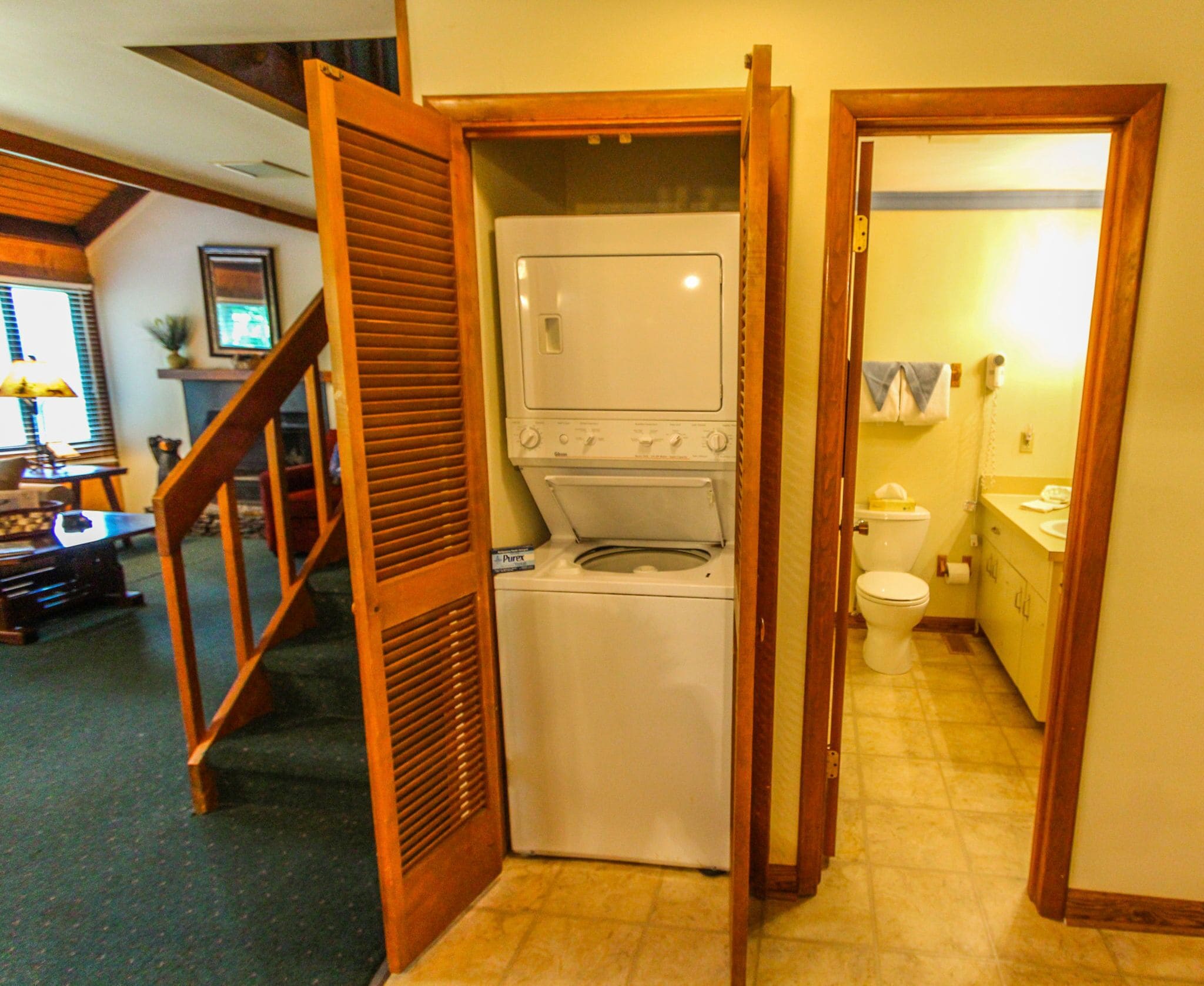 Ein Waschraum mit Waschmaschine und Trockner, eine Holztreppe und ein Badezimmer mit Toilette und Waschbecken.