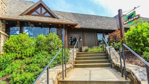 A building with a stone staircase leading to a wooden door, surrounded by greenery. - Mountain Condo w/ Deck & Fireplace (Marble Hill)