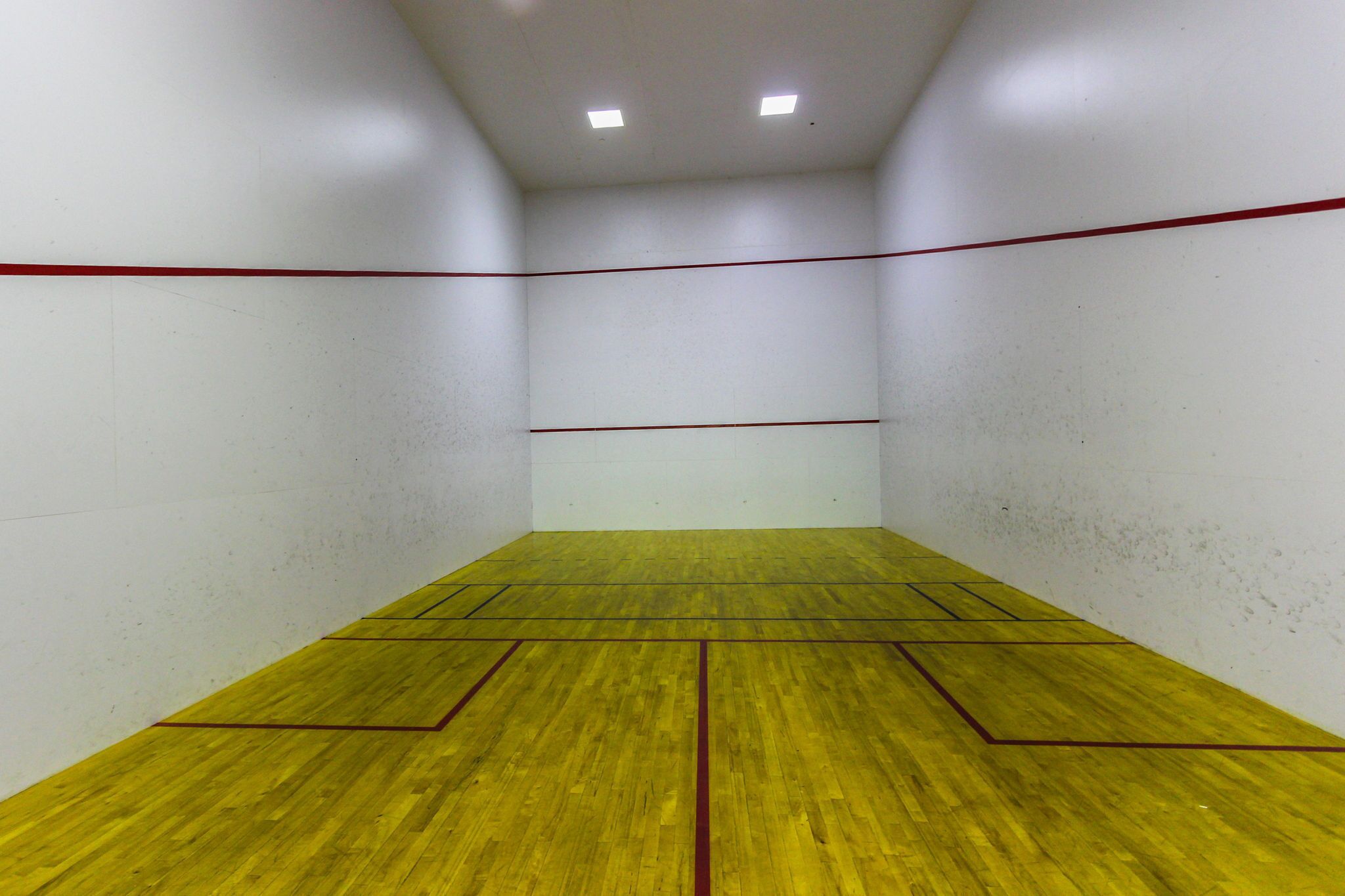 En squashhall med gult golv och röda linjer som markerar spelplanens gränser.