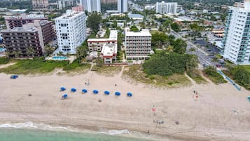 En vy över en strand, tagen från luften, med flera byggnader i bakgrunden, inklusive höga hotell och bostadshus.