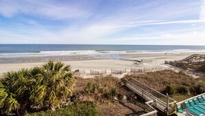 A beach with a wooden walkway leading to a sandy area, surrounded by vegetation.