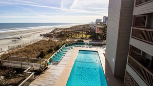 A swimming pool with a wooden deck, overlooking a beach and ocean.