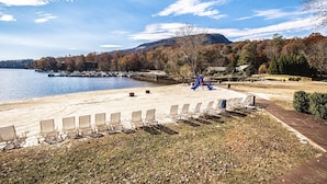 A lakeside beach with lounge chairs, a playground, and a dock with boats. - Mountain Retreat w/ Pools & Fireplace (Lake Lure)