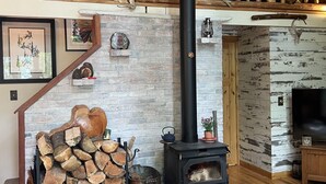 Una habitación acogedora con chimenea, leña, un hervidor y un televisor.
