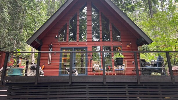 Una cabaña roja con ventanas grandes y un balcón, rodeada de árboles.