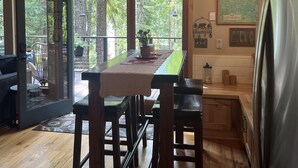 Una cocina amplia con ventanas grandes, taburetes de madera y un refrigerador de acero inoxidable.