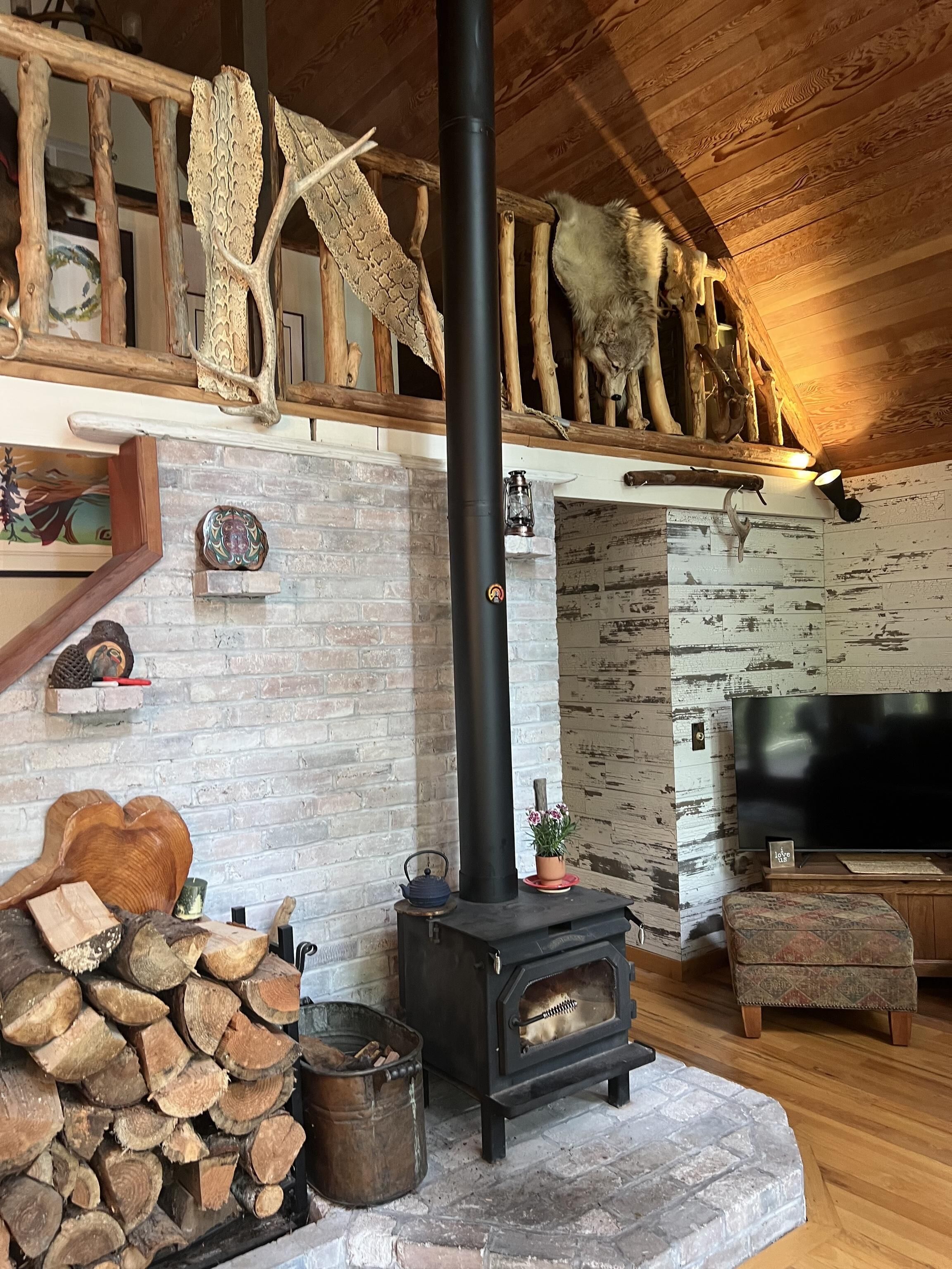 A rustic interior with a wooden ceiling, a stone fireplace, a television, and a wooden bench.