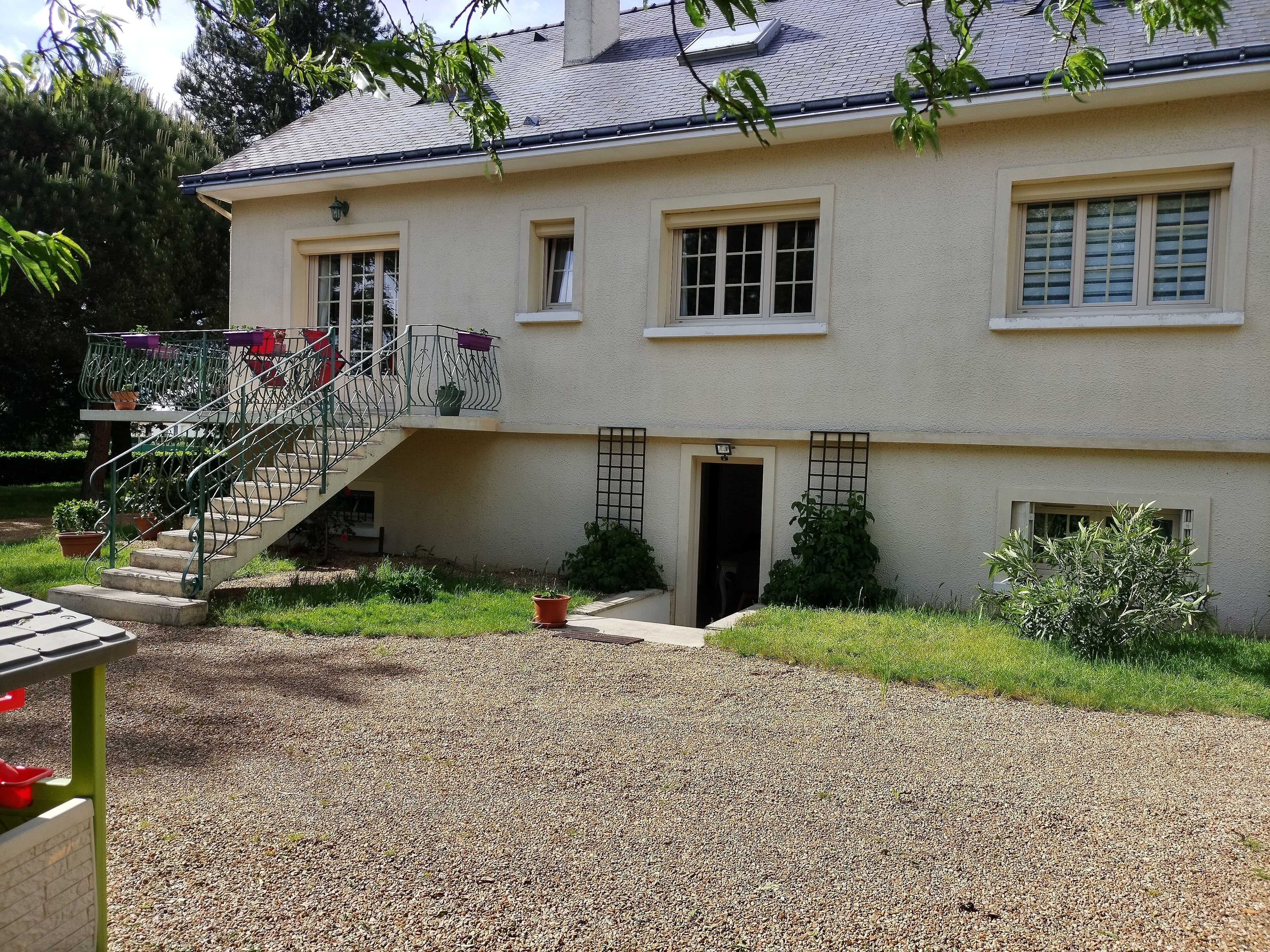 Une maison à deux étages avec une allée en gravier, un escalier doté de rampes et un petit jardin agrémenté de plantes en pot.