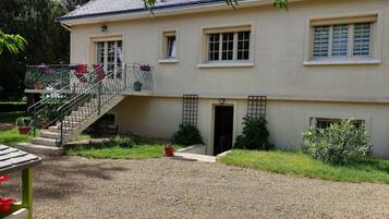 Une maison à deux étages avec une allée en gravier, un escalier doté de rampes et un petit jardin agrémenté de plantes en pot.