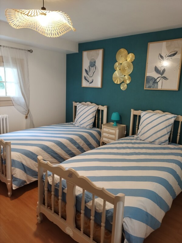 A bedroom with two beds, a nightstand, a lamp, and wall art.