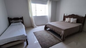 A bedroom with two single beds, a large window with curtains, and a wooden headboard.