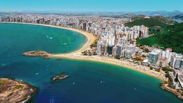 An aerial view of a coastal city with a beach, high-rise buildings, and a clear blue sky.