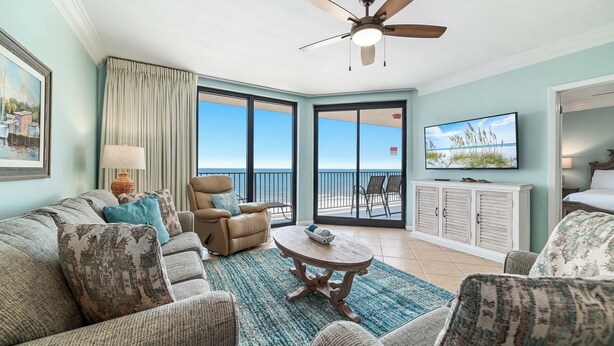 A living room with a ceiling fan, a sofa set, a coffee table, and a TV. - Phoenix X 803 | Beachfront | Next to Flora-Bama | Pools & Hot Tubs | My Beach Getaways (Orange Beach)