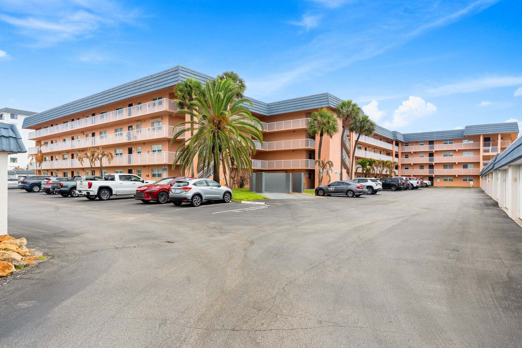 A multi-story hotel with a parking lot, palm trees, and a clear sky.