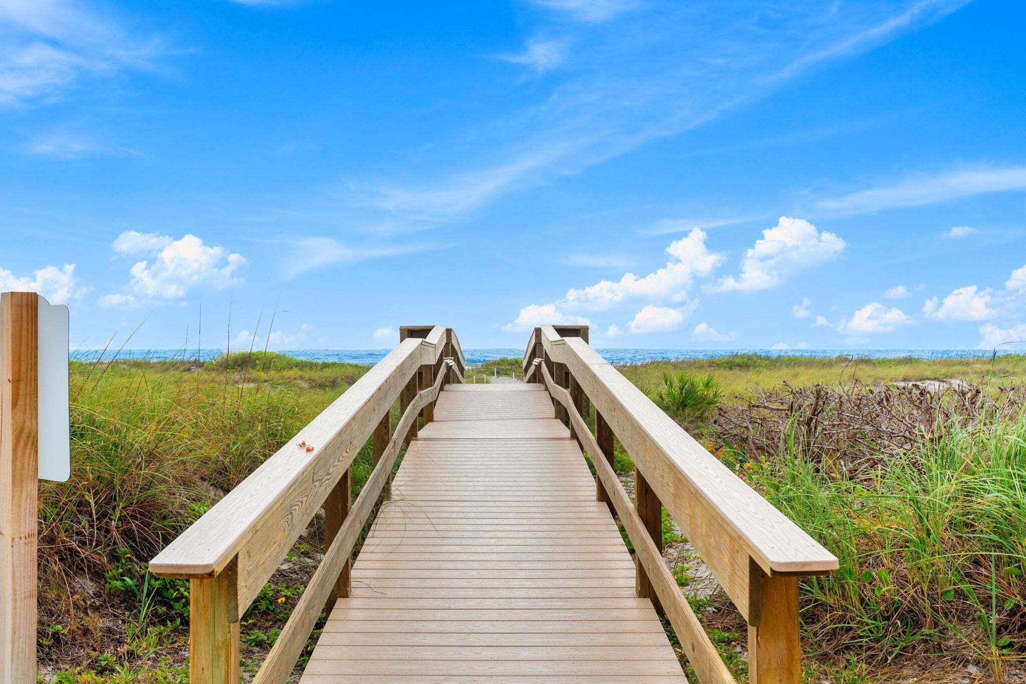 A wooden boardwalk leading to the beach with a clear sky.