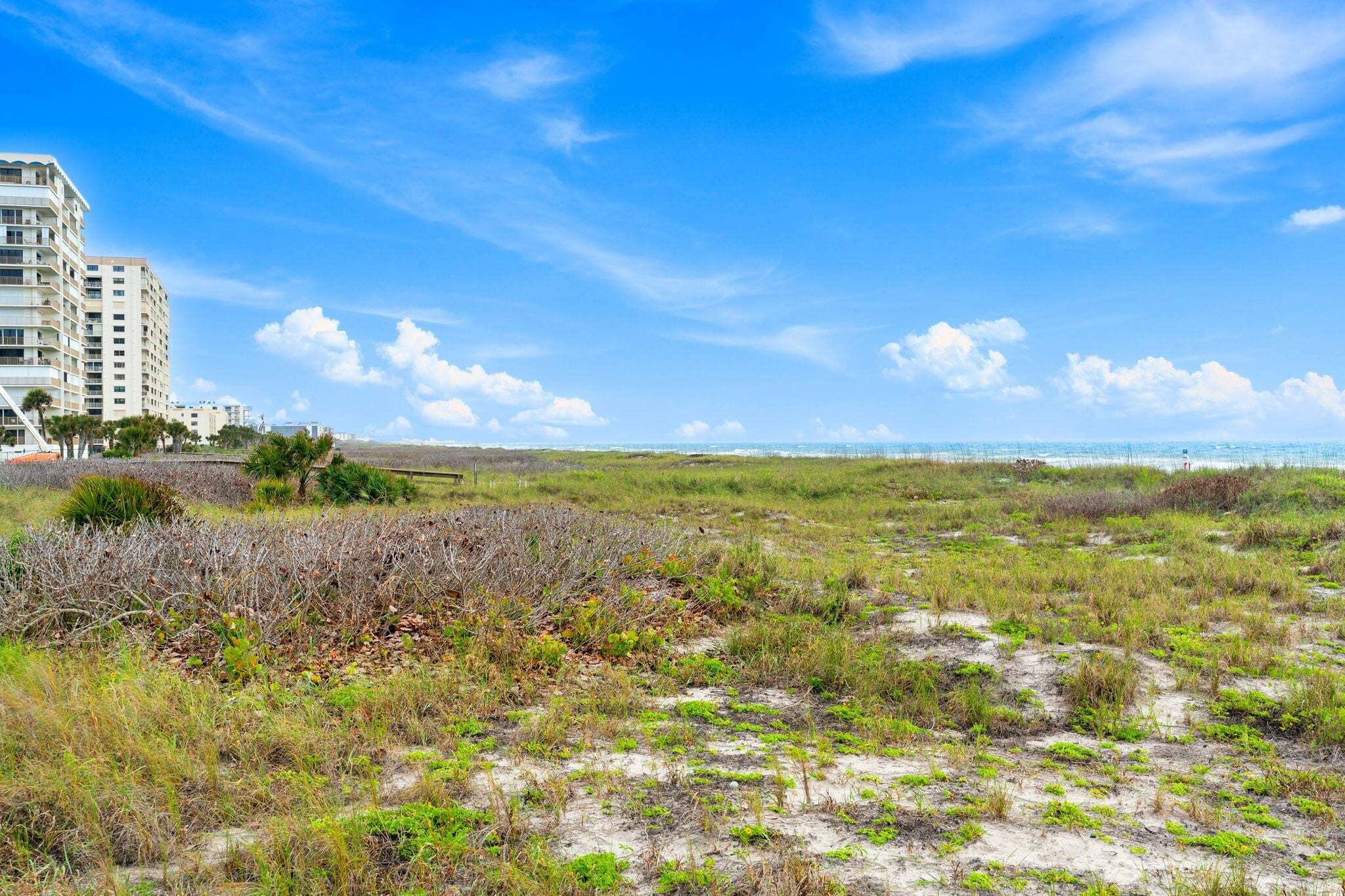 A coastal landscape with a building, sandy terrain, and sparse vegetation.