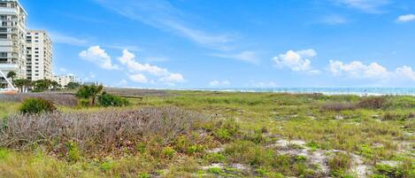 A coastal landscape with a building, sandy terrain, and sparse vegetation.