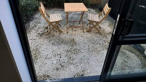 A patio with a wooden table and two chairs, a gravel ground, a wooden fence, and a building with windows in the background. - Downtown Cutie - Central City (Christchurch)