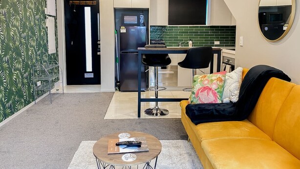 A modern living room with a yellow sofa, a coffee table, and a kitchen area in the background. - Downtown Cutie - Central City (Christchurch)