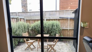 A sliding glass door leading to a patio with a wooden table and chairs, a wooden fence, and a small garden area. - Downtown Cutie - Central City (Christchurch)