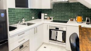A modern kitchen with white cabinets, a green-tiled backsplash, a Bosch oven, and a black chair. - Downtown Cutie - Central City (Christchurch)