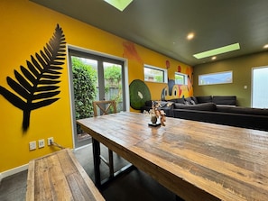 Un moderno salón con una gran mesa de madera, un sofá negro y un mural de colores.