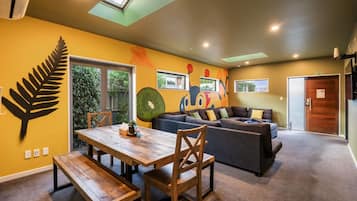 Un salon chaleureux avec une table à manger en bois, un canapé et une grande fenêtre donnant sur un espace verdoyant.