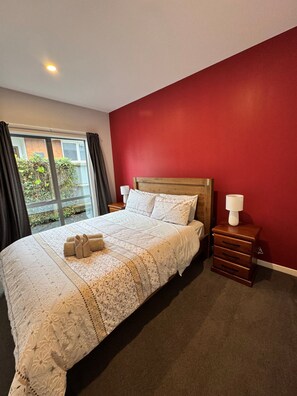 Habitación de hotel con una cama grande, una mesita de noche de madera, una pared roja y una ventana con cortinas.