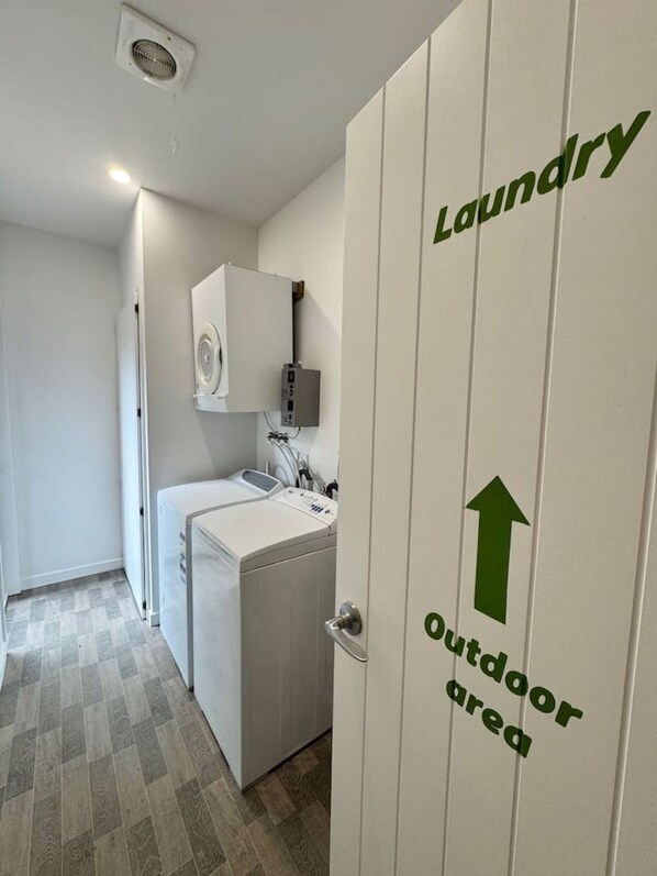 A laundry area with a washing machine and dryer, a small sink, and a mirror. There is a door with an arrow pointing to the outdoor area.