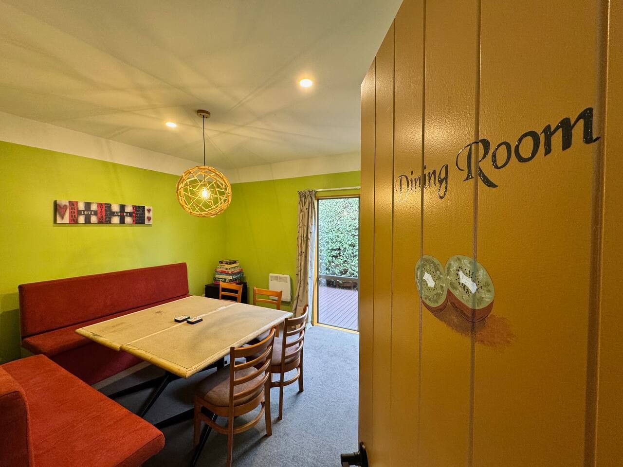 A dining room with a table, chairs, a red sofa, and a wall with a 'Dining Room' sign.