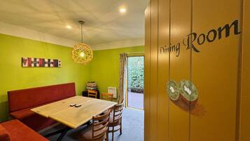 A dining room with a table, chairs, a red sofa, and a wall with a 'Dining Room' sign.